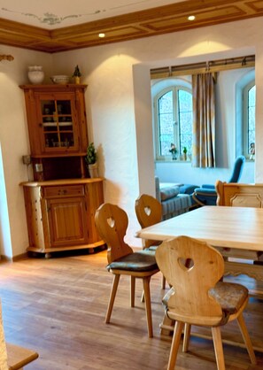 Ein Essbereich mit Holztischen und -stühlen, einem Holzschrank mit Glastüren und einem mit Vorhängen drapierten Fenster.