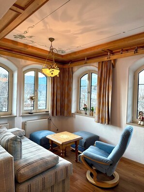 Ein gemütliches Zimmer mit Holzbalkendecke, einem blauen Sessel, einer Couch und einem Tisch.