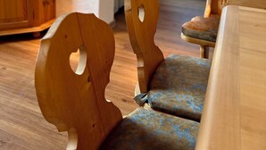 Een houten stoel met een opvallend rugontwerp, een beklede bank en een houten kast in een kamer met een groot raam en uitzicht op het omliggende landschap.