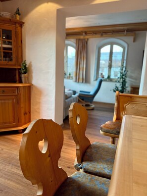 Ein Holzstuhl mit außergewöhnlichem Rückenlehndesign, eine gepolsterte Bank und ein Holzschrank in einem Raum mit einem großen Fenster und Blick ins Freie.