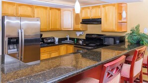 A kitchen with wooden cabinets, a stainless steel refrigerator, a stove, a microwave, and a water dispenser. - One Bedroom Suite (Freeport)