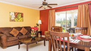 A living room with a brown sofa, a dining table set for two, and a ceiling fan. - One Bedroom Suite (Freeport)
