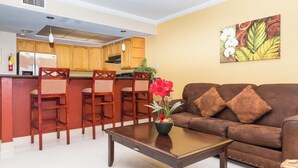 A living room with a brown sofa, a coffee table with a vase of flowers, and wooden chairs. - One Bedroom Suite (Freeport)