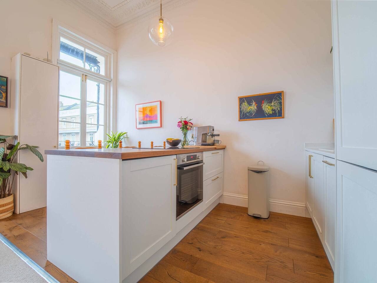 A kitchen with white cabinetry, a wooden countertop, a built-in oven, a trash bin, and artwork on the walls.