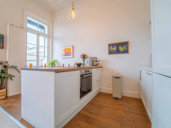 A kitchen with white cabinetry, a wooden countertop, a built-in oven, a trash bin, and artwork on the walls.