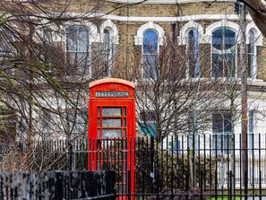 A red telephone booth in front of a brick building with arched windows.