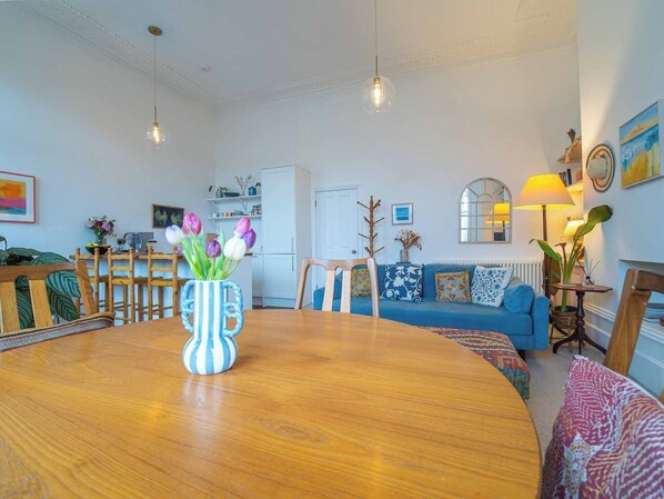 A dining area with a wooden table, a vase with flowers, a blue sofa, and a wooden chair.