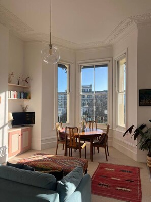 Una habitación con una mesa de comedor, sillas, un sofá, un televisor y una estantería.