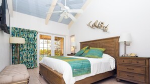 A bedroom with a bed, bedside tables, a nightstand, a chair, a ceiling fan, and a window with curtains. - Three Bedroom Townhouse (Freeport)