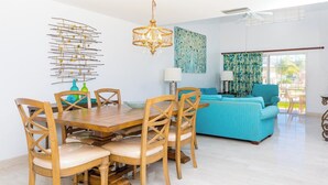 A dining area with a wooden table and chairs, a chandelier, and a blue sofa in the background. - Three Bedroom Townhouse (Freeport)