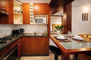 A modern kitchen with wooden cabinets, a microwave, a sink, and a dining area with a glass table and chairs. - Bellas Artes and Lastarrias Apartments (Santiago)