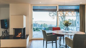 Uma sala de estar moderna com lareira, uma mesa de jantar com cadeiras e uma grande porta de vidro que dá para uma varanda.
