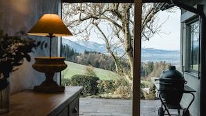 Vista de um quarto com luminária e churrasqueira, com vista para uma paisagem com árvores e montanhas.