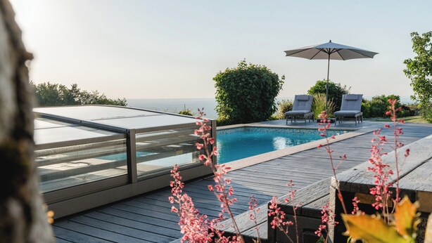 Uma piscina com deck de madeira, duas espreguiçadeiras e um guarda-sol.