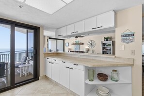 A modern kitchen with white cabinets, a large window, and a view of the sea. - Sherwin Condominium 901 (Daytona Beach Shores)