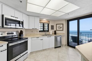 A modern kitchen with stainless steel appliances, a dishwasher, and a large window overlooking the ocean. - Sherwin Condominium 901 (Daytona Beach Shores)