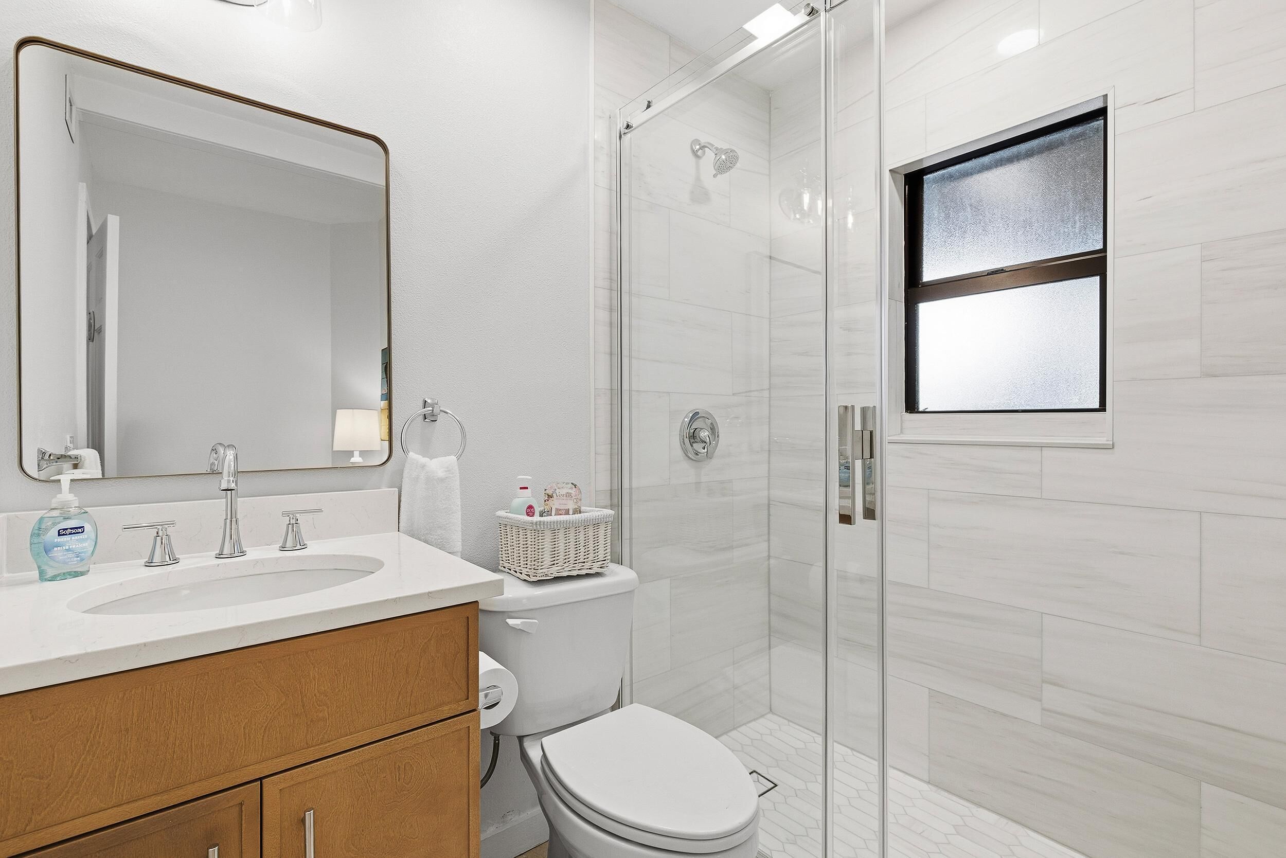 A modern bathroom with a large mirror, a sink, a toilet, and a shower.
