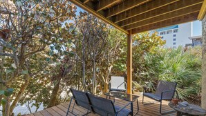 An outdoor patio with wooden flooring, two black chairs, a glass table, and a potted plant.