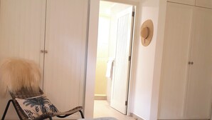 Un dormitorio con una cama, una silla con almohada de hoja de palma y una pila de toallas.
