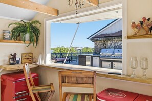 Ein Zimmer mit einem Holzstuhl, einem roten, alten Kühlschrank, einem Fenster mit Blick auf eine Grillanlage im Freien und einem Regal mit Dekoration.
