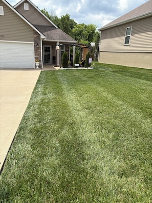 A residential lawn with a garage, a covered patio, and a small garden area with potted plants. - 2 bdrm - Condo in Independence, MO close to Chiefs stadium / World Cup, coolAC, (Independence)