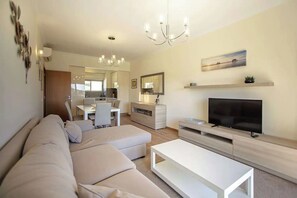 A modern living room with a sofa, TV, and a dining area in the background. - Elegant and cocooning in a luxury residence near the Marina (Albufeira)