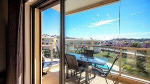A balcony with a glass door, a table with chairs, and a view of a residential area with buildings and a swimming pool. - Elegant and cocooning in a luxury residence near the Marina (Albufeira)