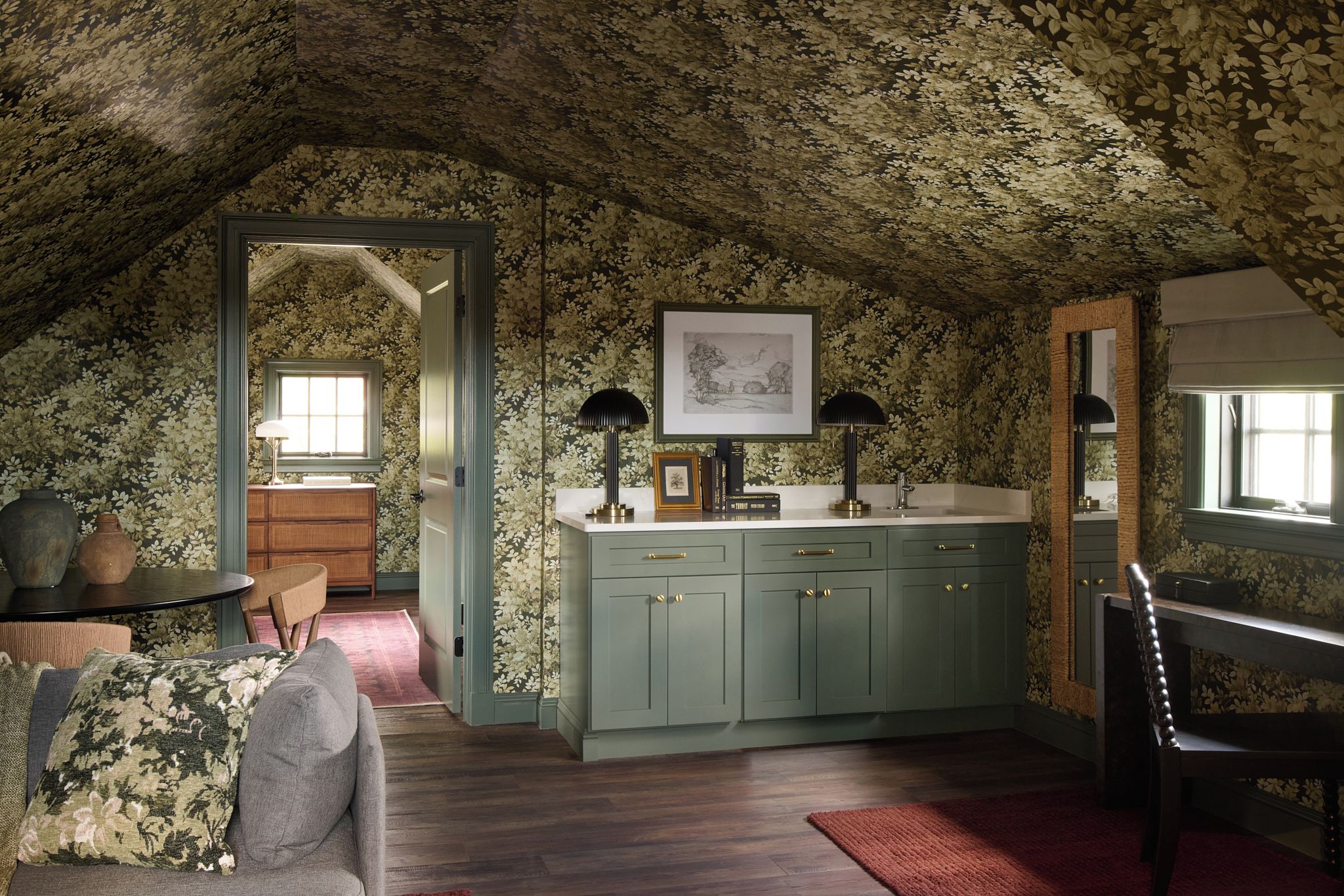 Ein Zimmer mit schräg stehender Decke, einem eingebauten Schrank mit Schubladen, einem gerahmten Bild an der Wand und einem Fenster.