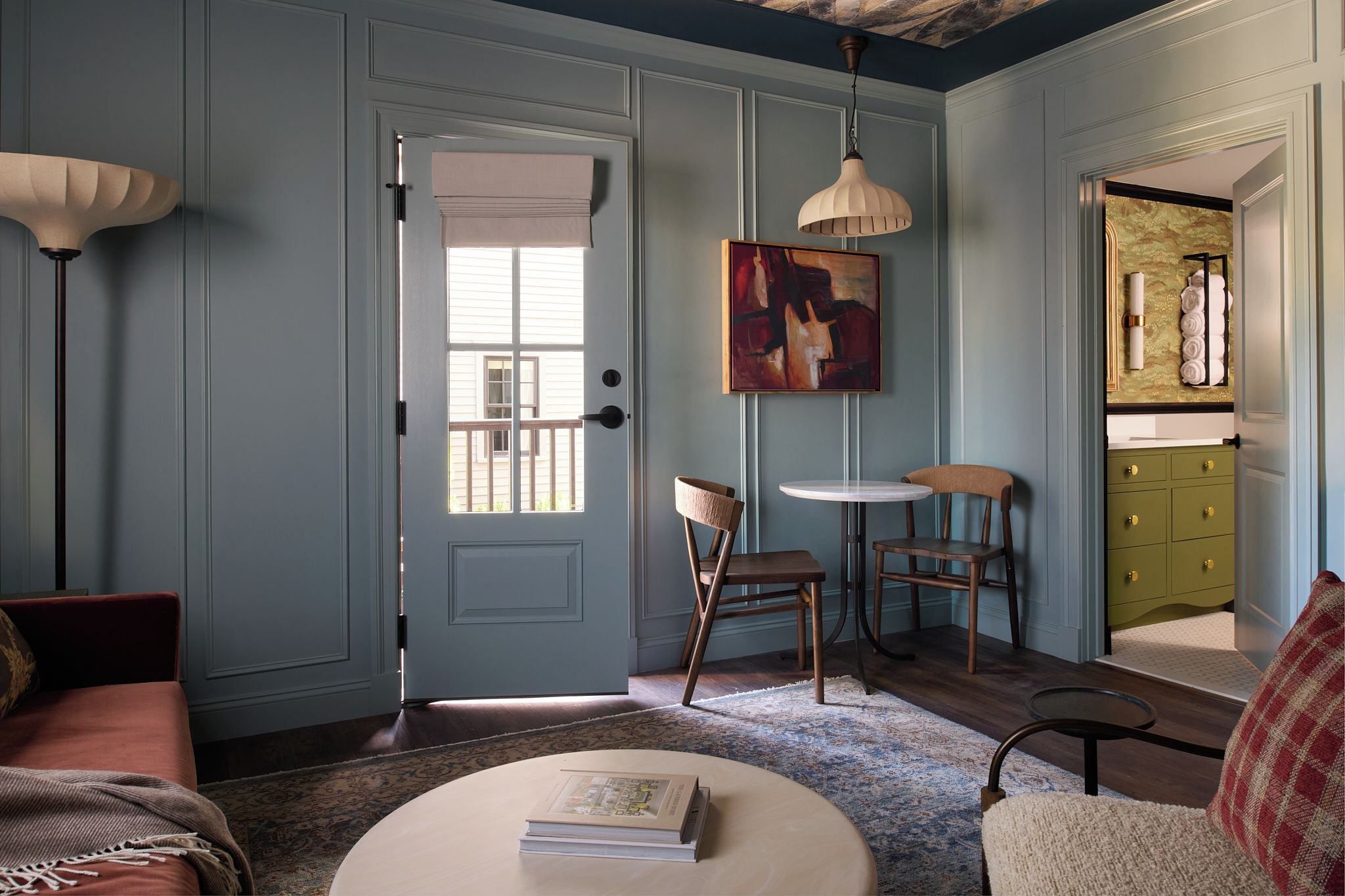 Una habitación con puerta, un cuadro, dos sillas, una mesa y un sofá.