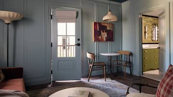 Una habitación con puerta, un cuadro, dos sillas, una mesa y un sofá.