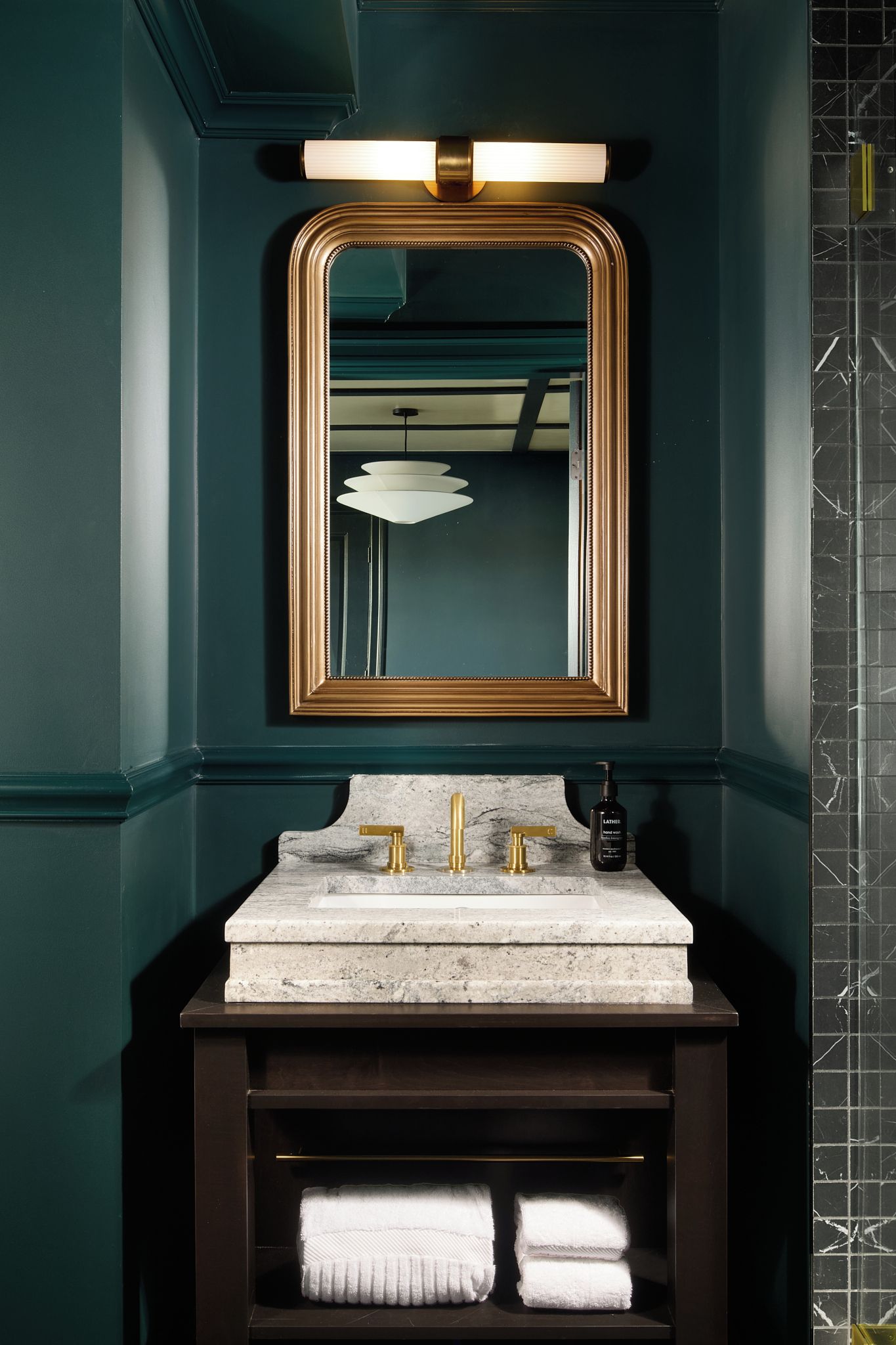 A bathroom with a marble sink, gold faucets, a large mirror, and a towel rack.