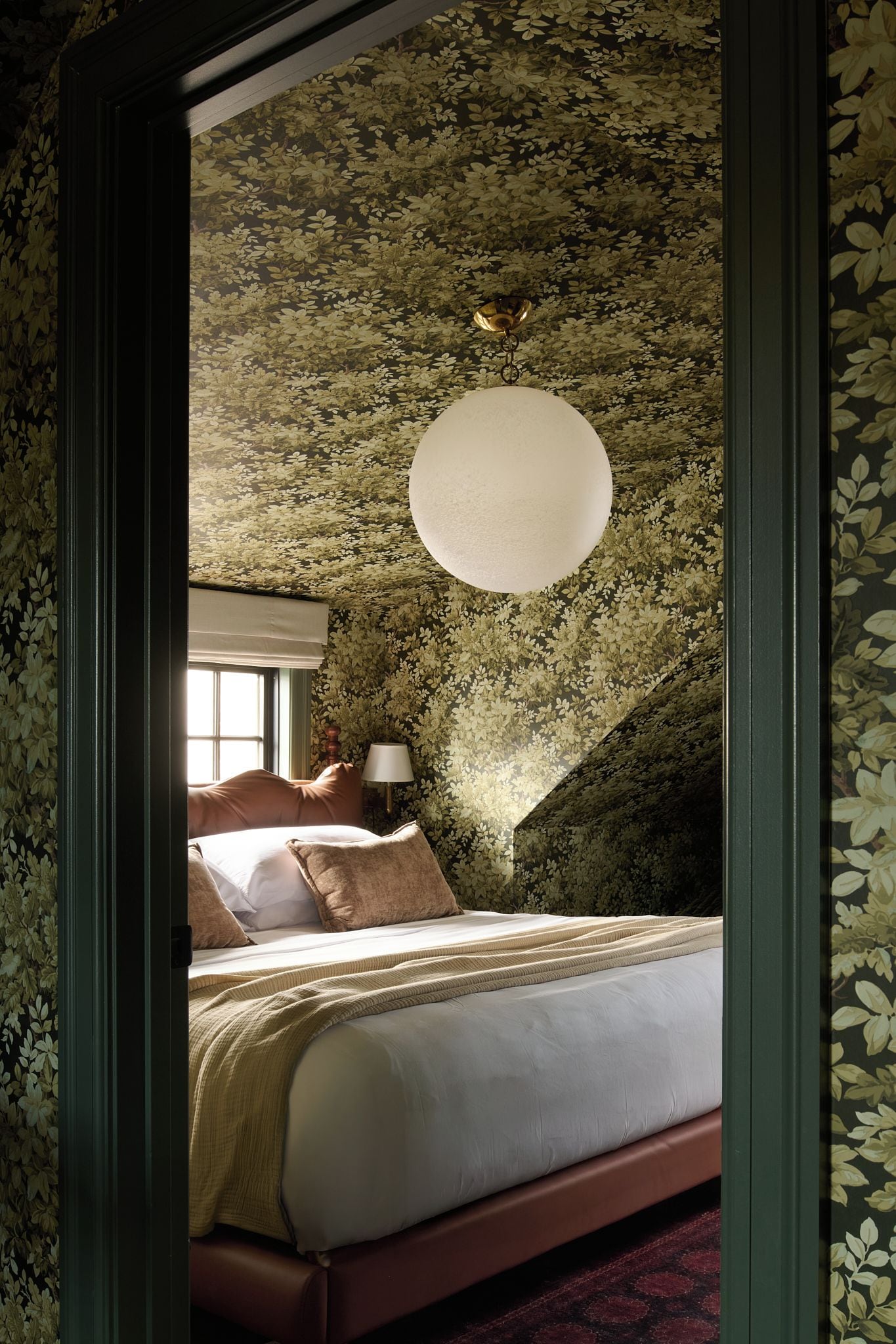 A bedroom with a large bed, a hanging light fixture, and a window.