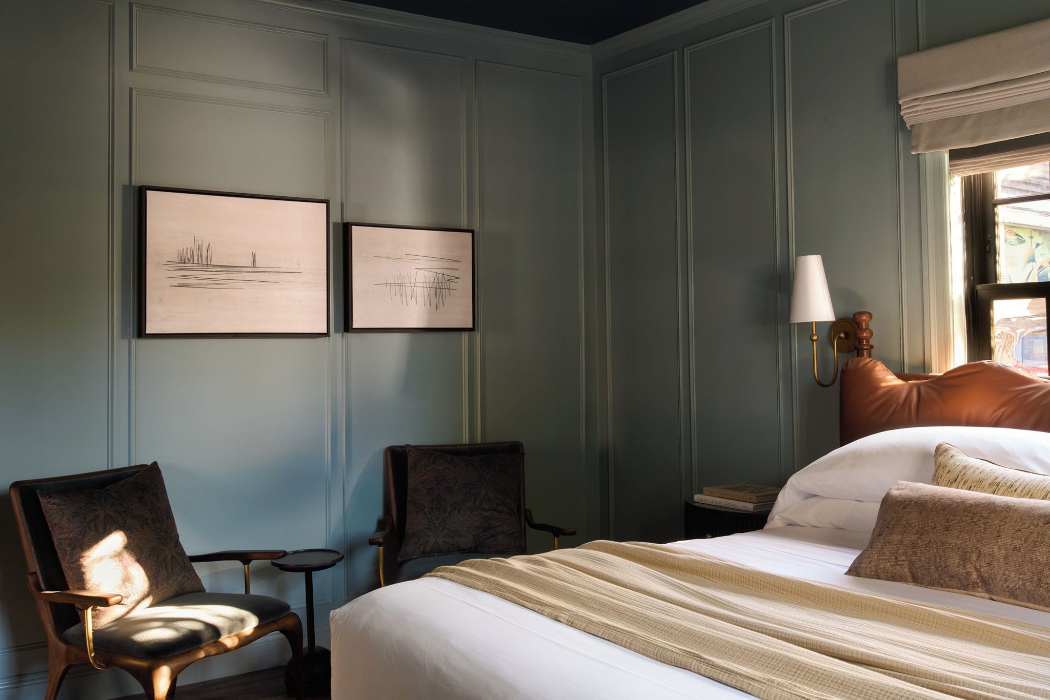 Habitació d'hotel amb un llit gran, dos seients, una tauleta de nit, una làmpada i dues obres d'art emmarcades a la paret.