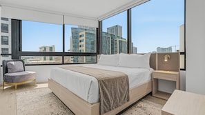 A modern hotel room with a large bed, a chair, a nightstand, and a view of the cityscape through large windows. - RS Suites - District 225 Miami (Miami)