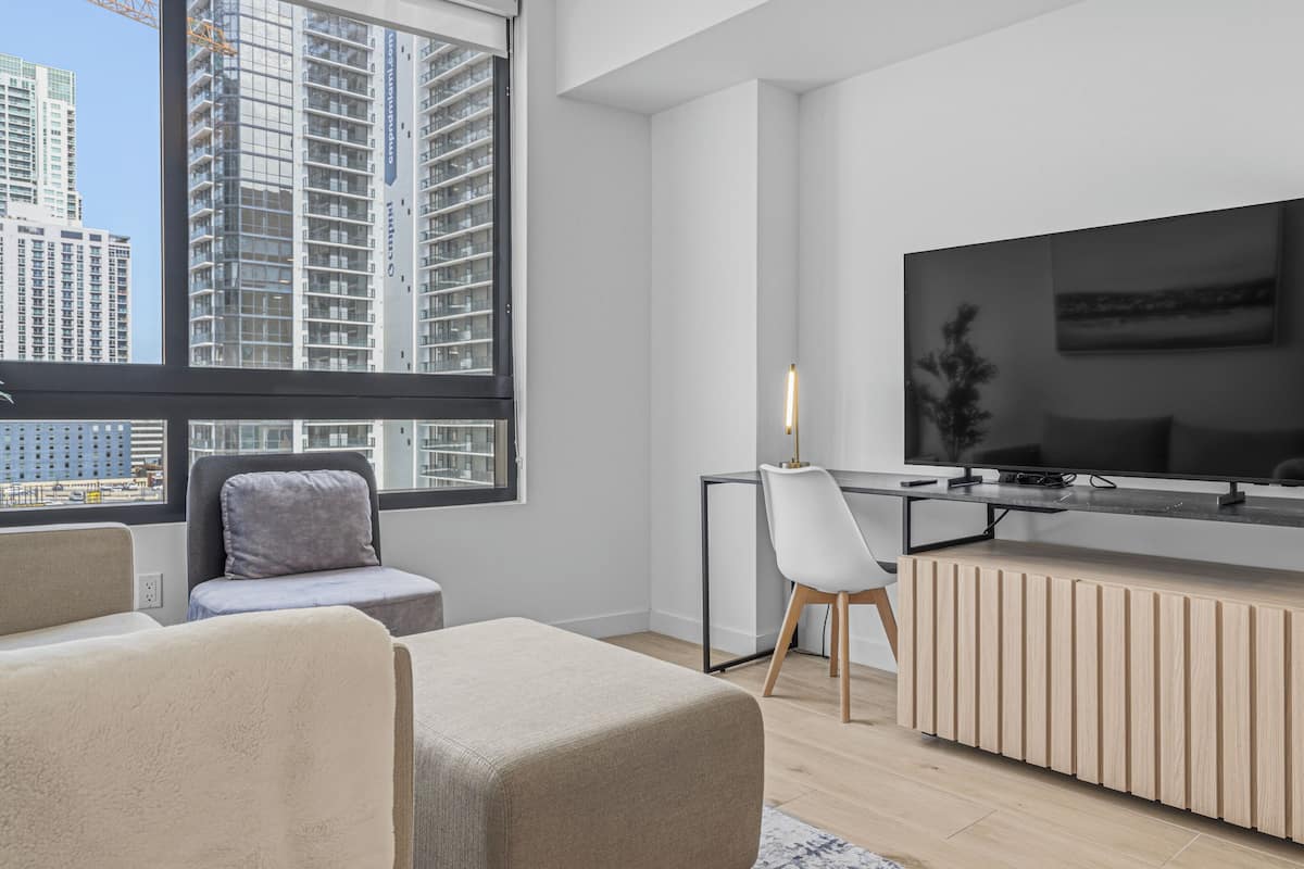 A modern living room with a large TV, a desk, and a comfortable seating area.