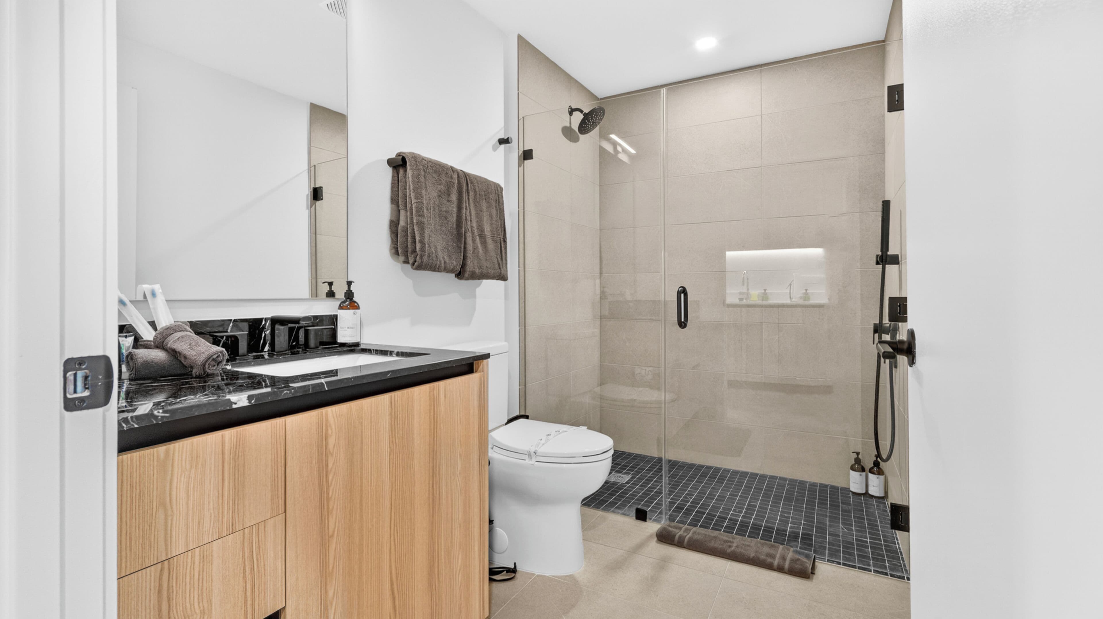 Un bagno moderno con cabina doccia in vetro, un mobile vanitario in legno, un water bianco e uno specchio.