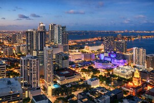 Paisagem urbana com edifícios altos, uma orla marítima e áreas iluminadas, sugerindo um ambiente citadino movimentado.