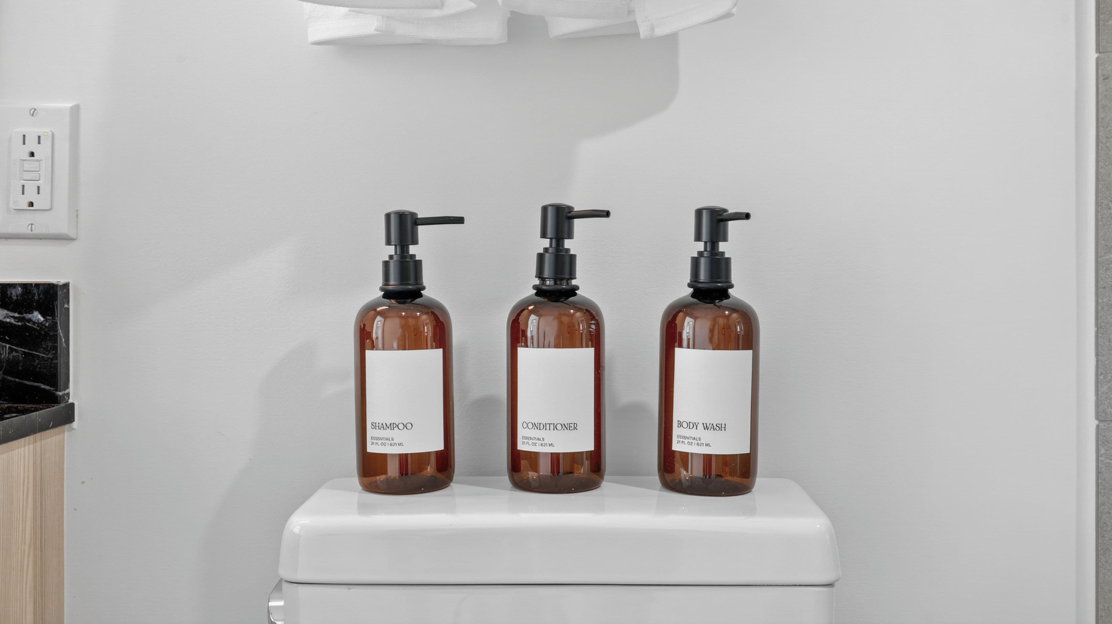 Tres botellas de champú, acondicionador y gel de ducha sobre un inodoro blanco.