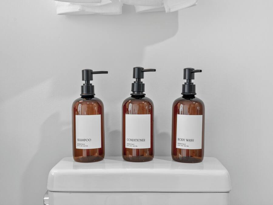 Three bottles of shampoo, conditioner, and body wash on a white toilet.