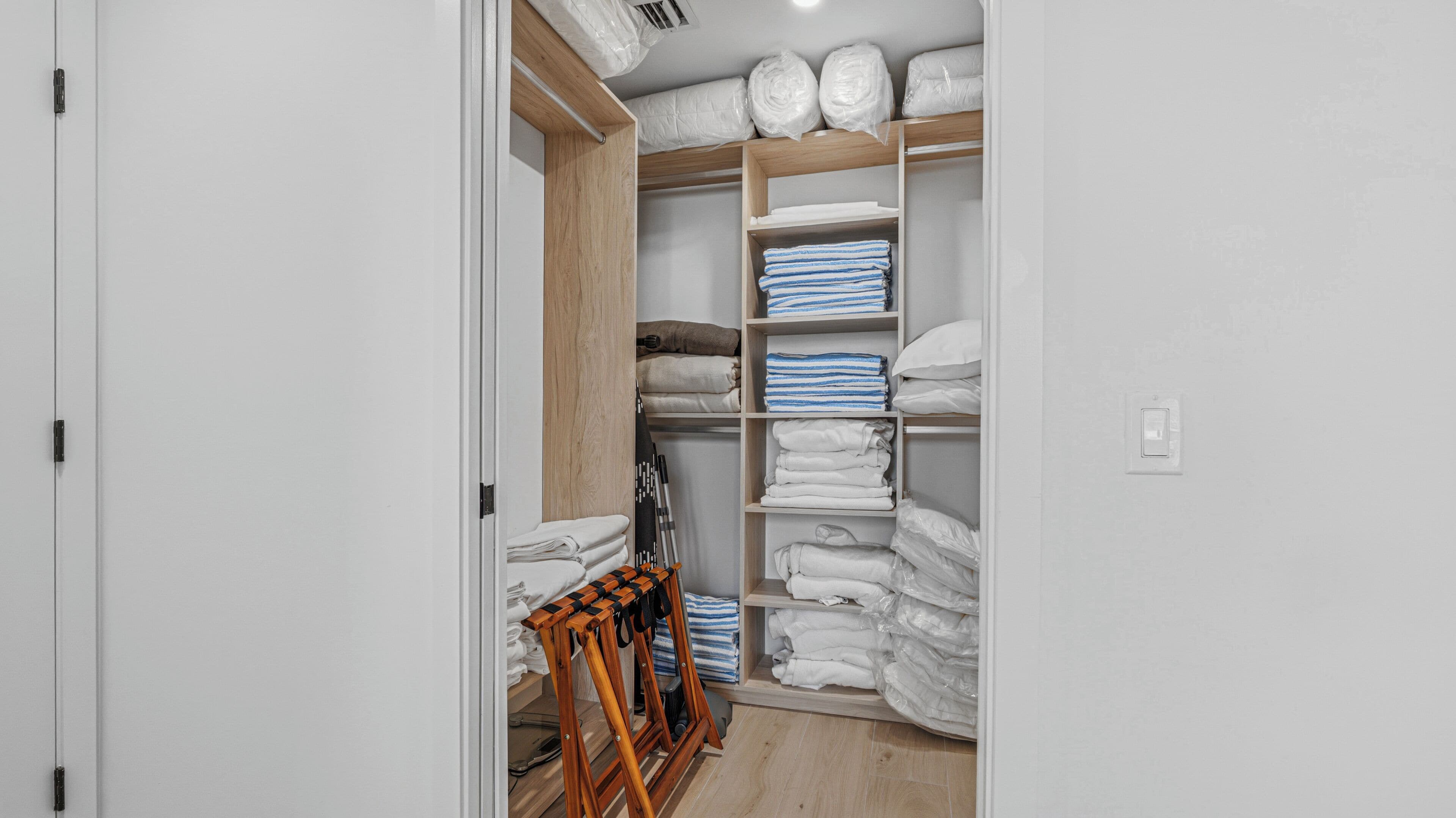 A walk-in closet with wooden shelves, a folding chair, and neatly stacked towels.