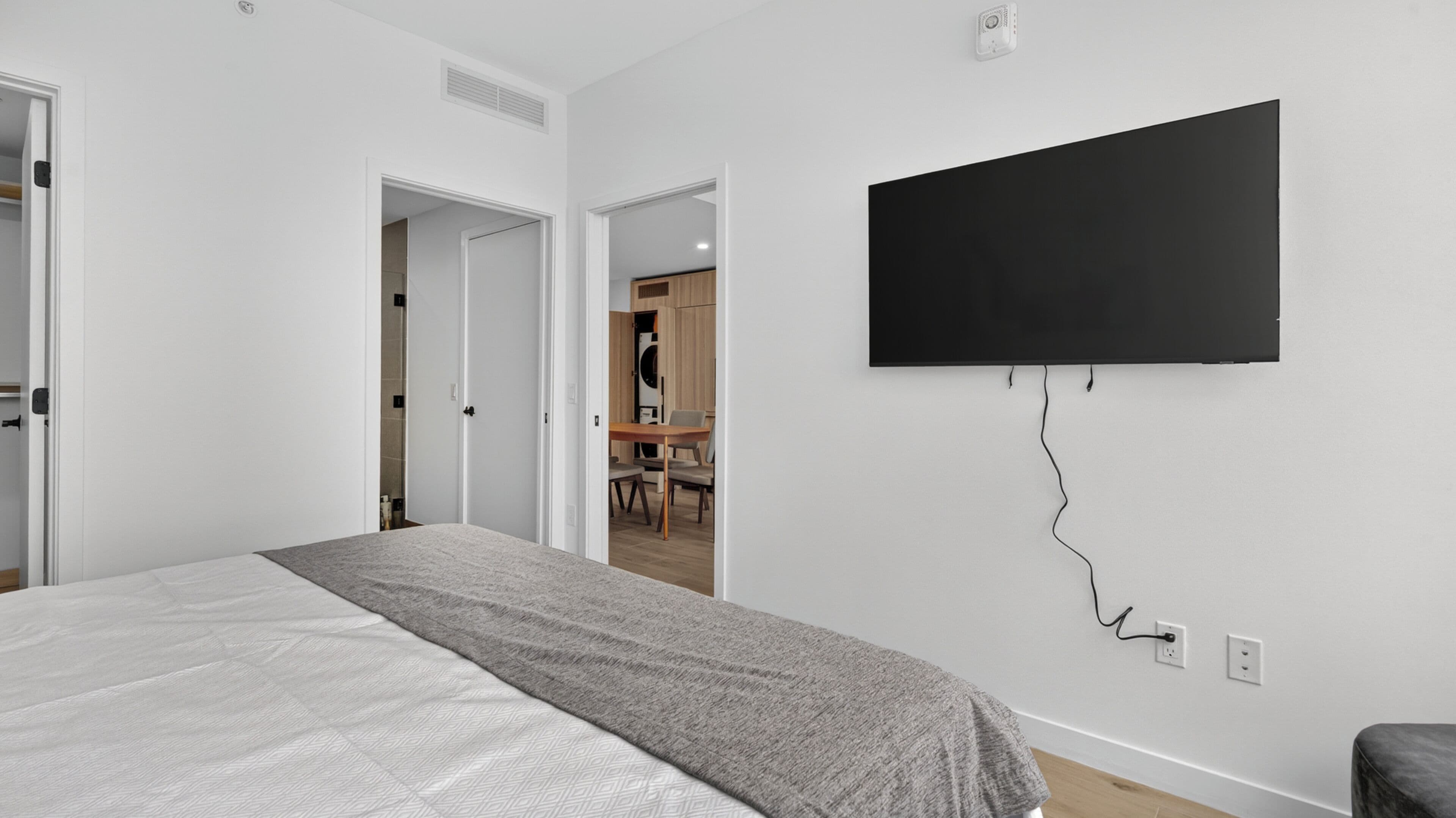 Quarto com uma cama, televisão na parede e porta para um banheiro.