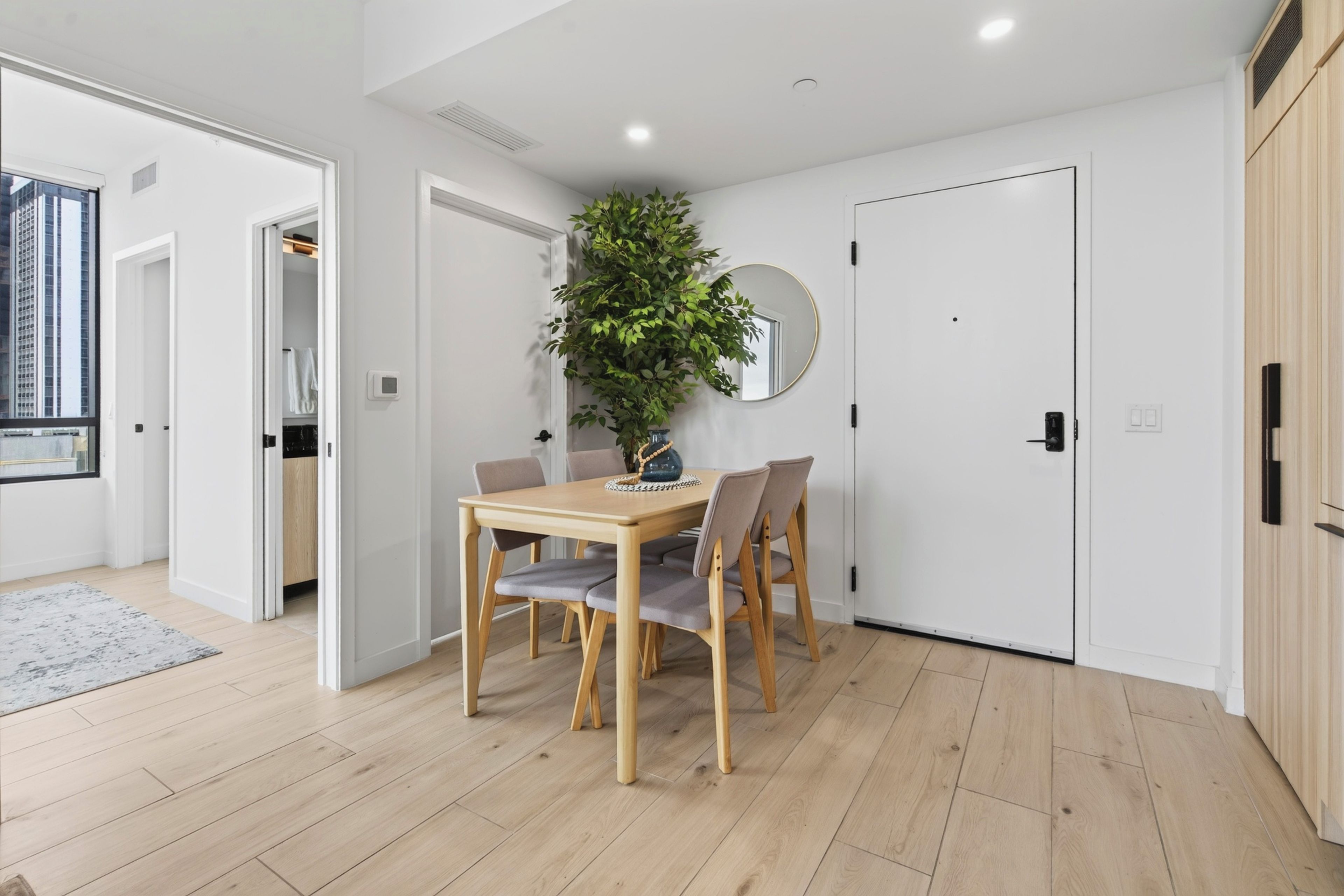 Un intérieur moderne avec une table à manger en bois, des chaises, une plante en pot et un miroir rond accroché au mur.