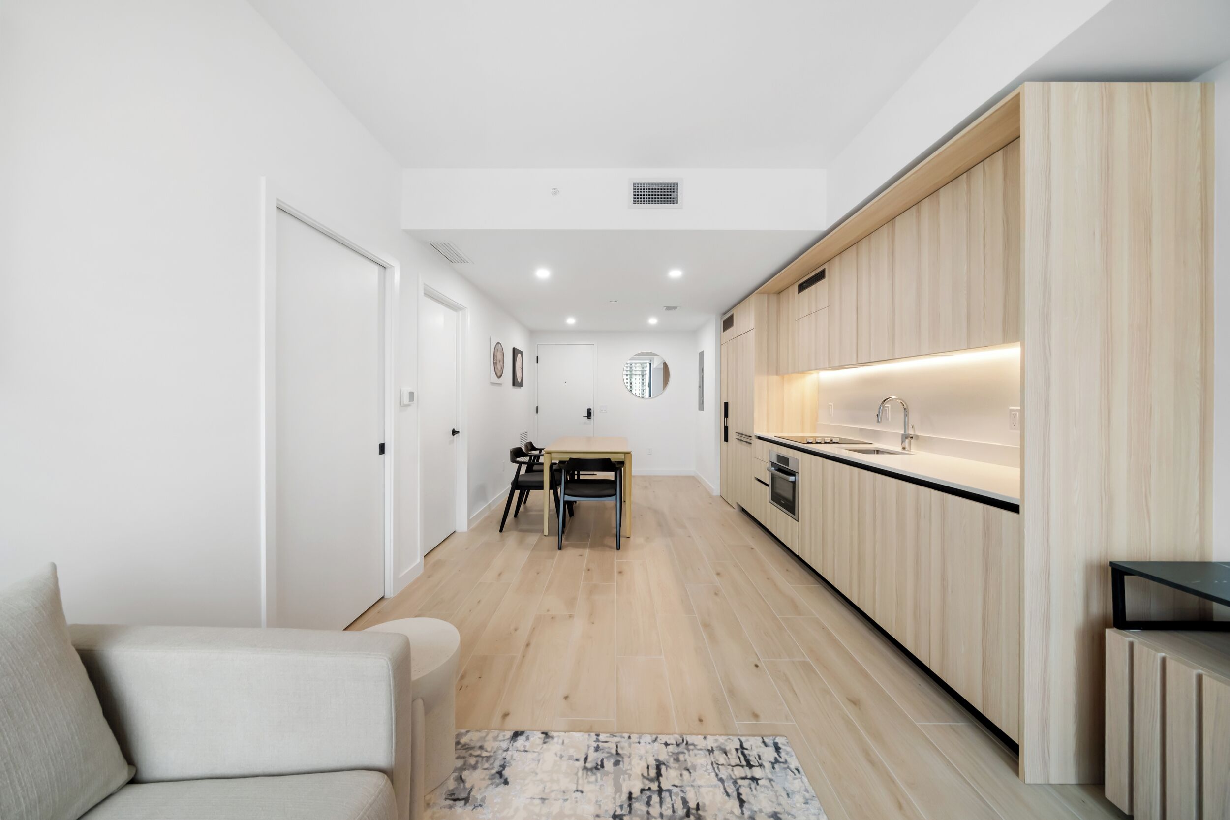 Una cocina moderna con armarios de madera, un comedor con mesa y sillas, y un piso de color claro.