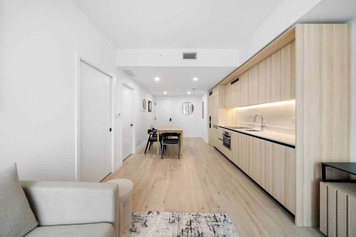 A modern kitchen with wooden cabinets, a dining area with a table and chairs, and a light-colored floor.