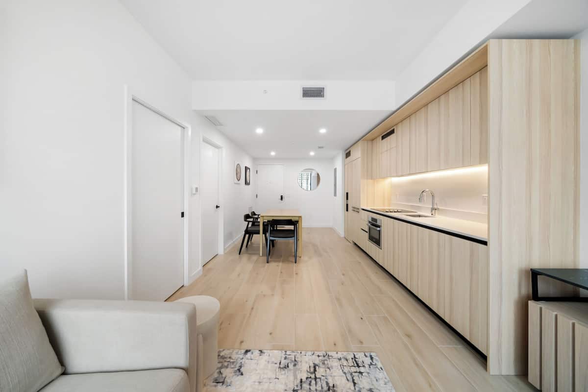 Una cocina moderna con armarios de madera, un comedor con mesa y sillas, y un piso de color claro.