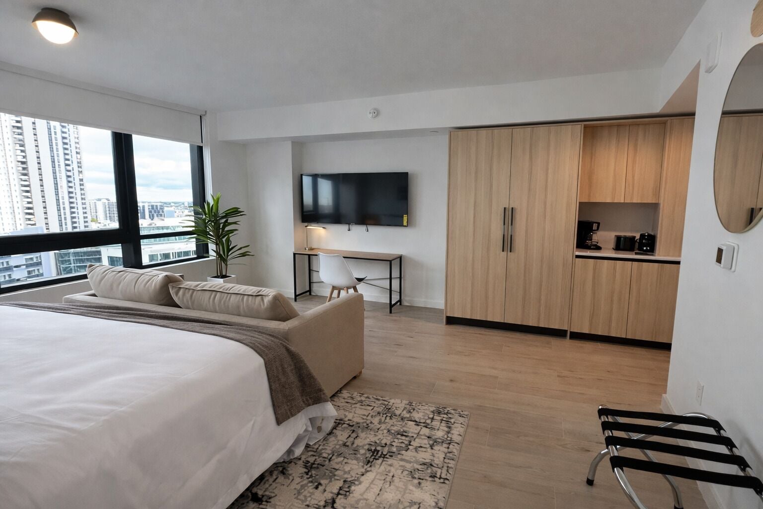 Un dormitorio moderno con una cama grande, un escritorio, un televisor y una kitchenette.
