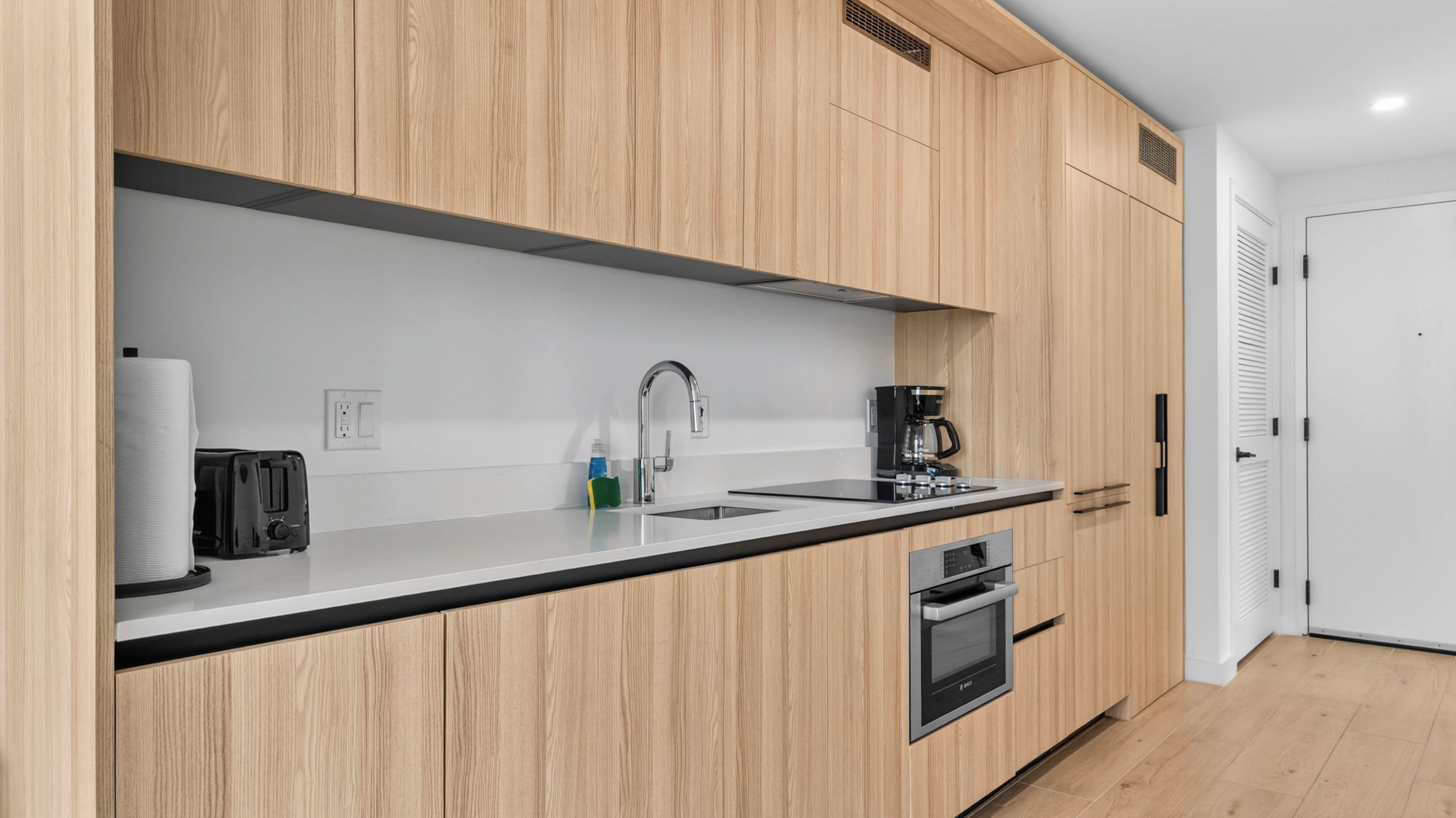 Eine moderne Küche mit Holzschränken, einer Edelstahl-Spüle, einer Kaffeemaschine, einem Toaster und einem Backofen.