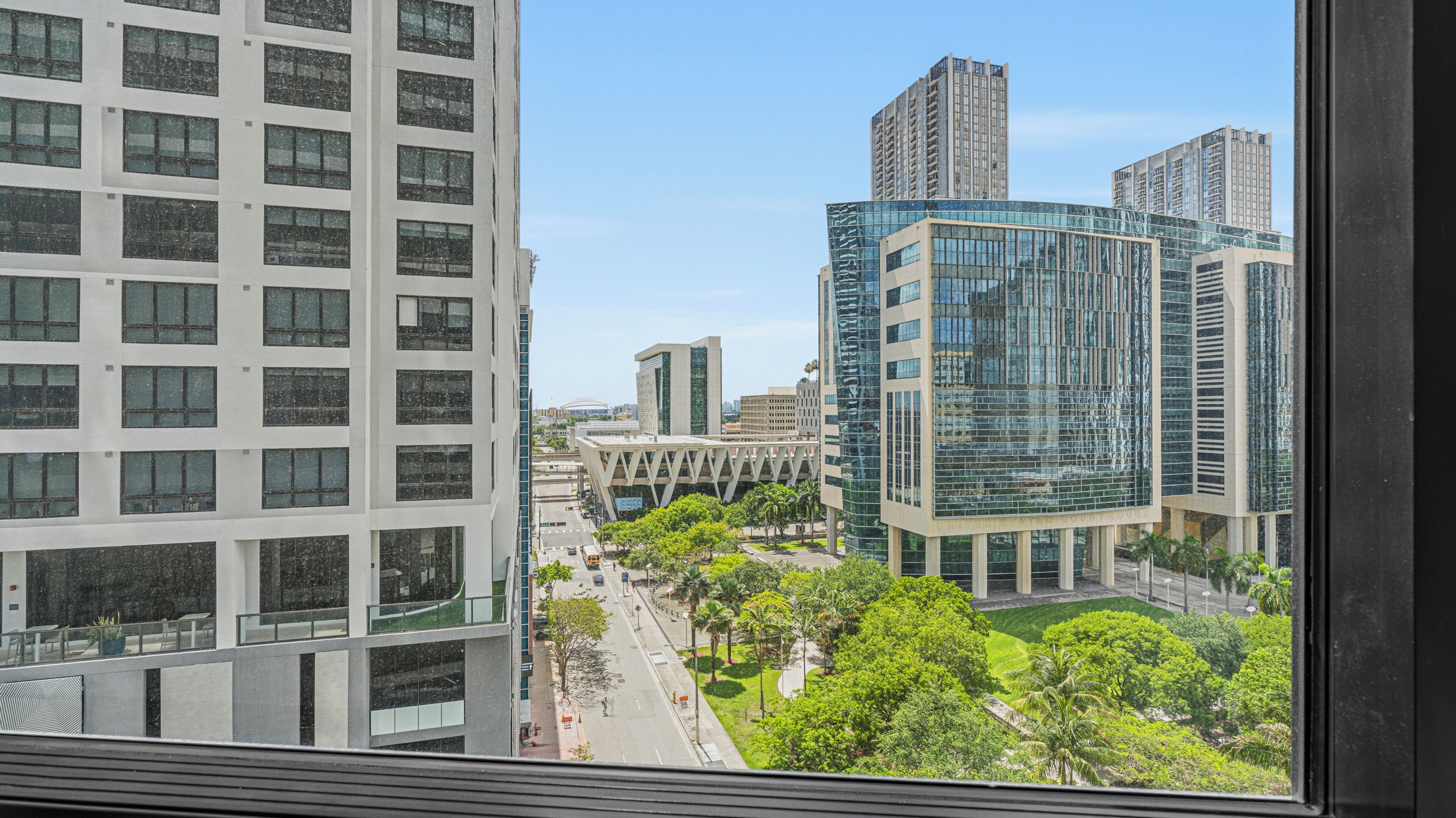 A high-rise building with a modern glass facade, a parking lot, and a green area with trees.
