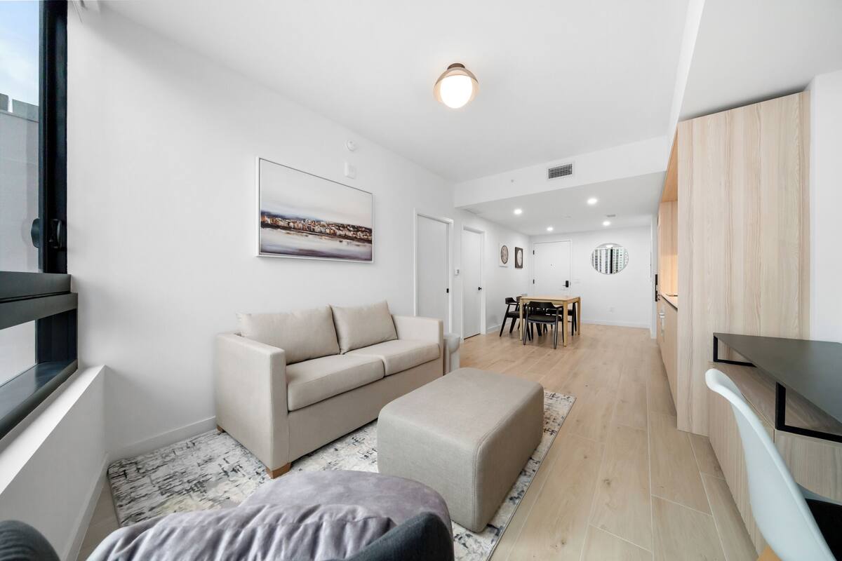 A modern living room with a sofa, ottoman, and a dining area with a table and chairs.