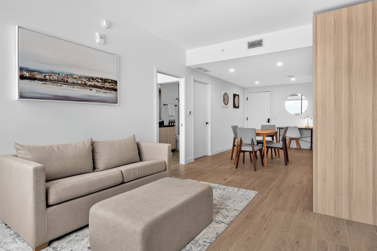 A modern living room with a sofa, a dining area with chairs and a table, and a kitchen in the background.
